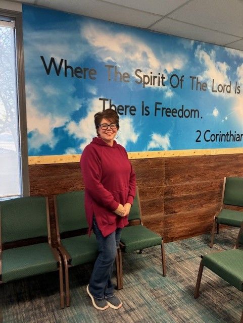Woman standing in a room with chairs and a wall mural that says 