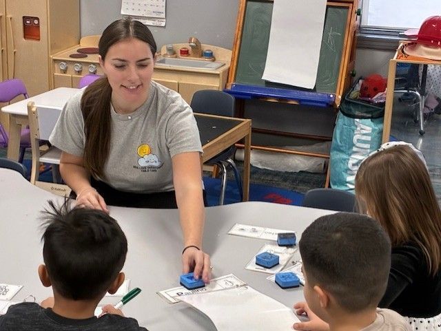 Children's classroom with tables, toys, and window. Blue and tan color scheme.