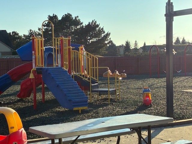 Playground with blue, red, and yellow equipment, picnic table, and swing set on a sunny day.