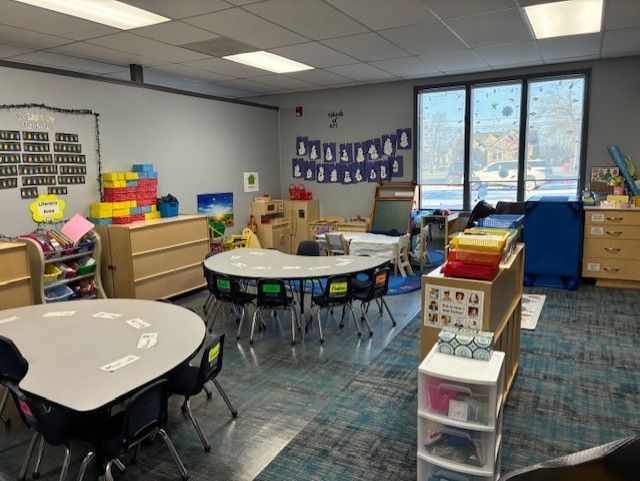 A preschool classroom with tables, chairs, toys, storage, and a large window.