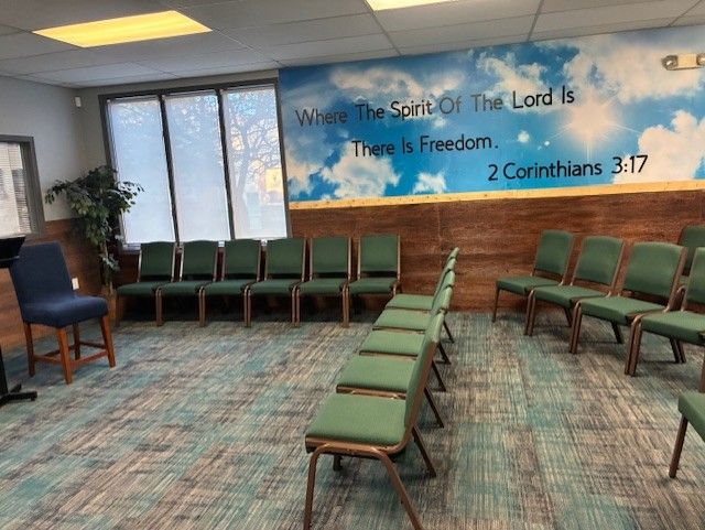 Empty chairs in a room with a scripture quote on the wall; blue, green, and brown tones.
