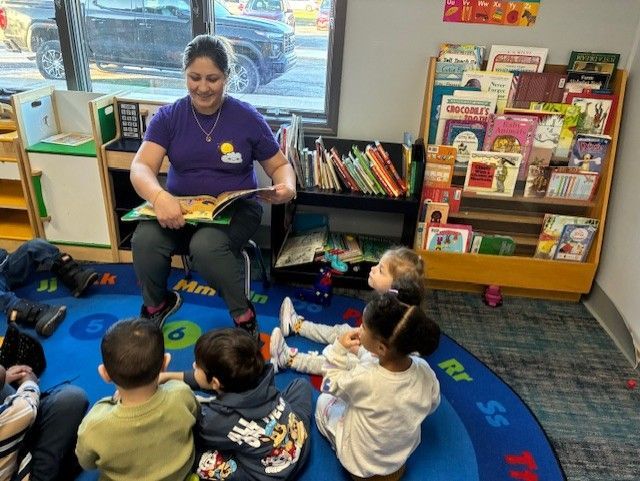 Teacher reads to children seated on a rug in a classroom.