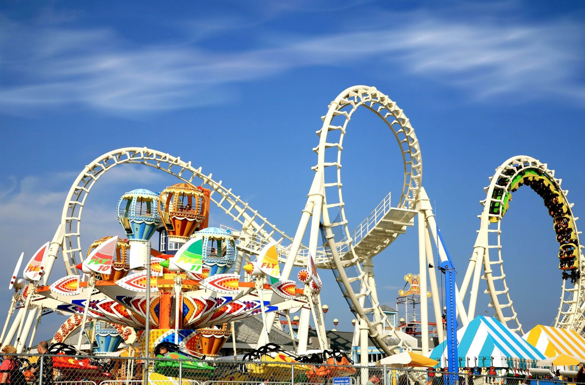 Amusement park with a colorful spinning ride and a roller coaster against a blue sky.