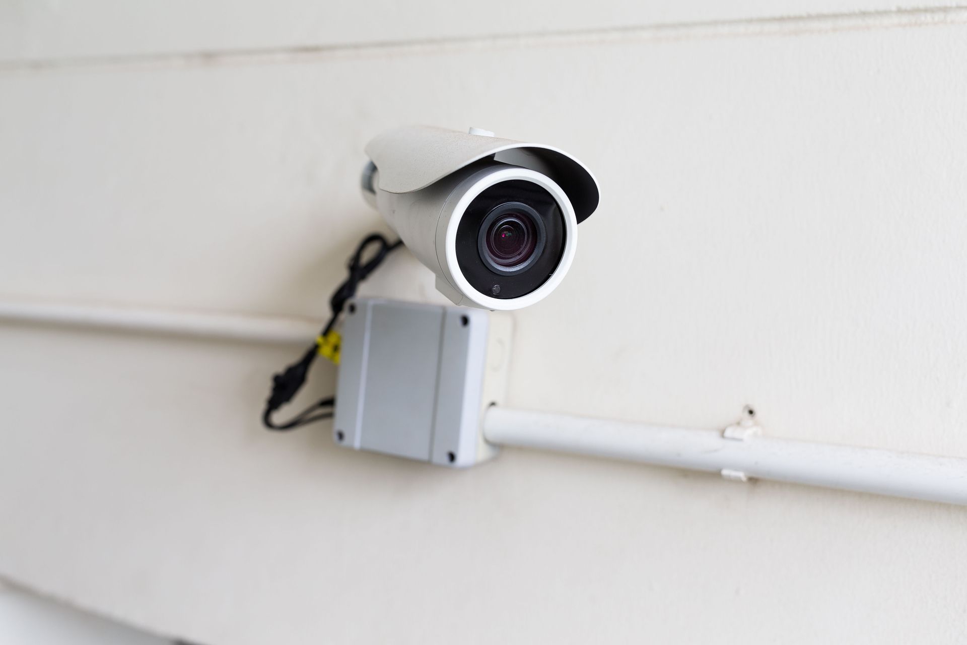 Outdoor security camera mounted on a white wall with conduit wiring.