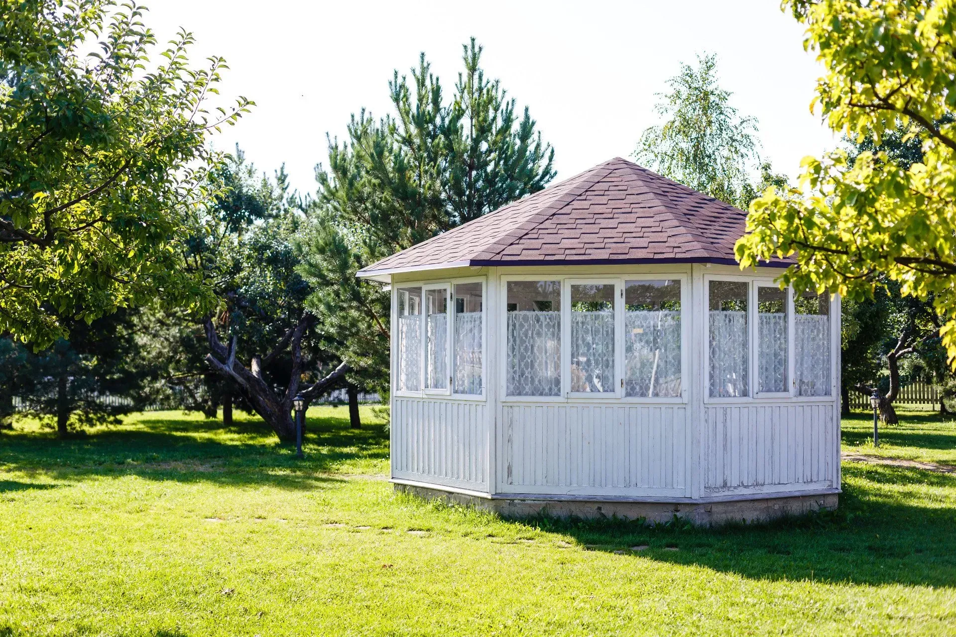 White gazebo with pink roof in a sunny green park surrounded by trees