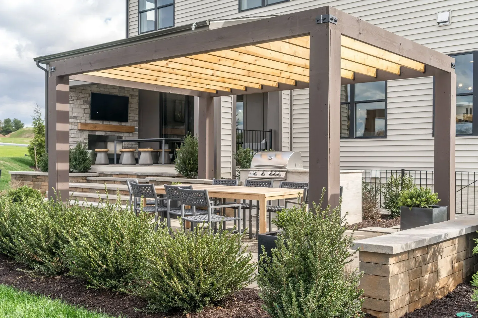 Modern backyard patio with a pergola, outdoor seating, and a built-in grill by a house