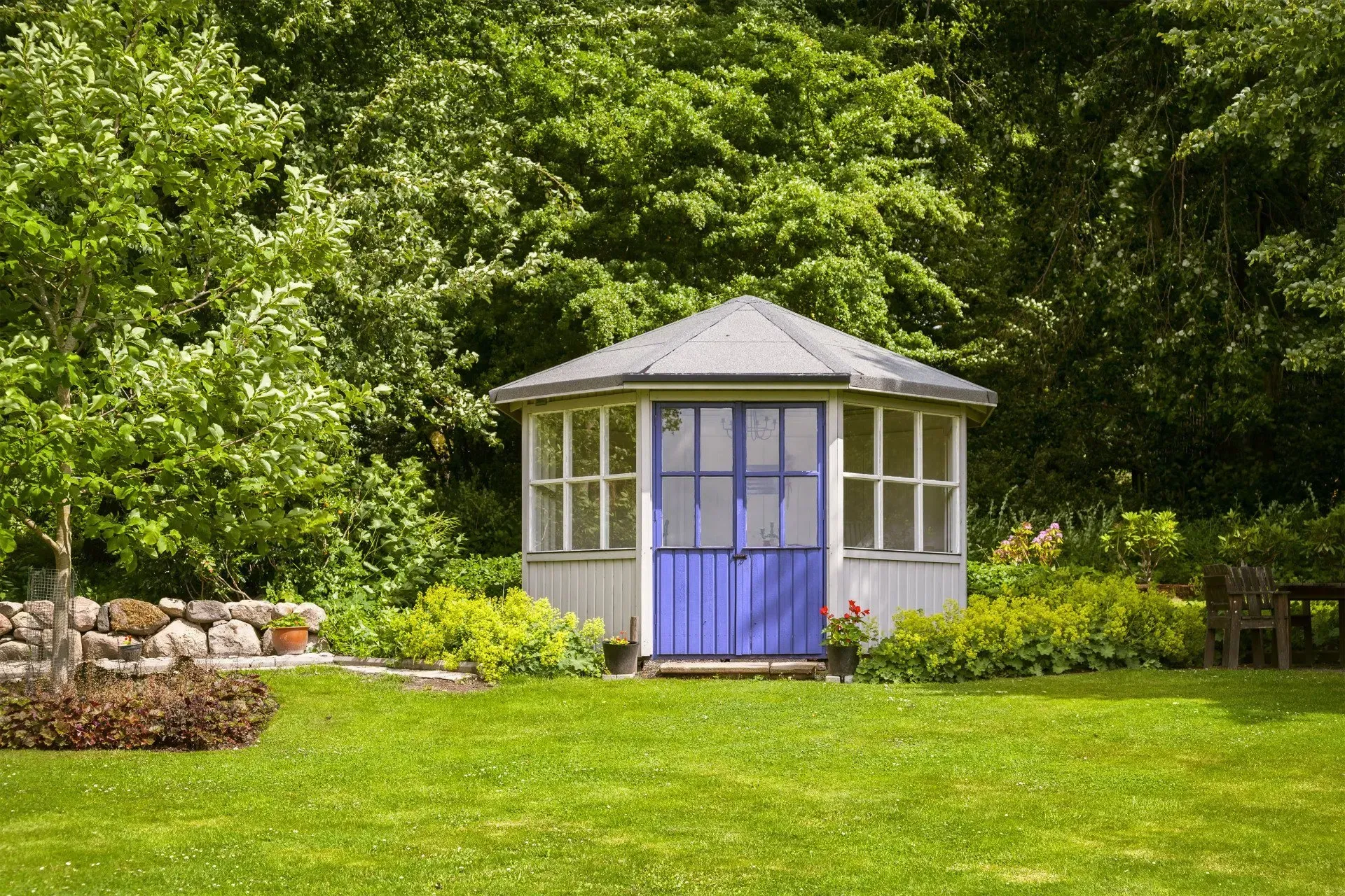 Small white gazebo with a blue door in a lush green garden