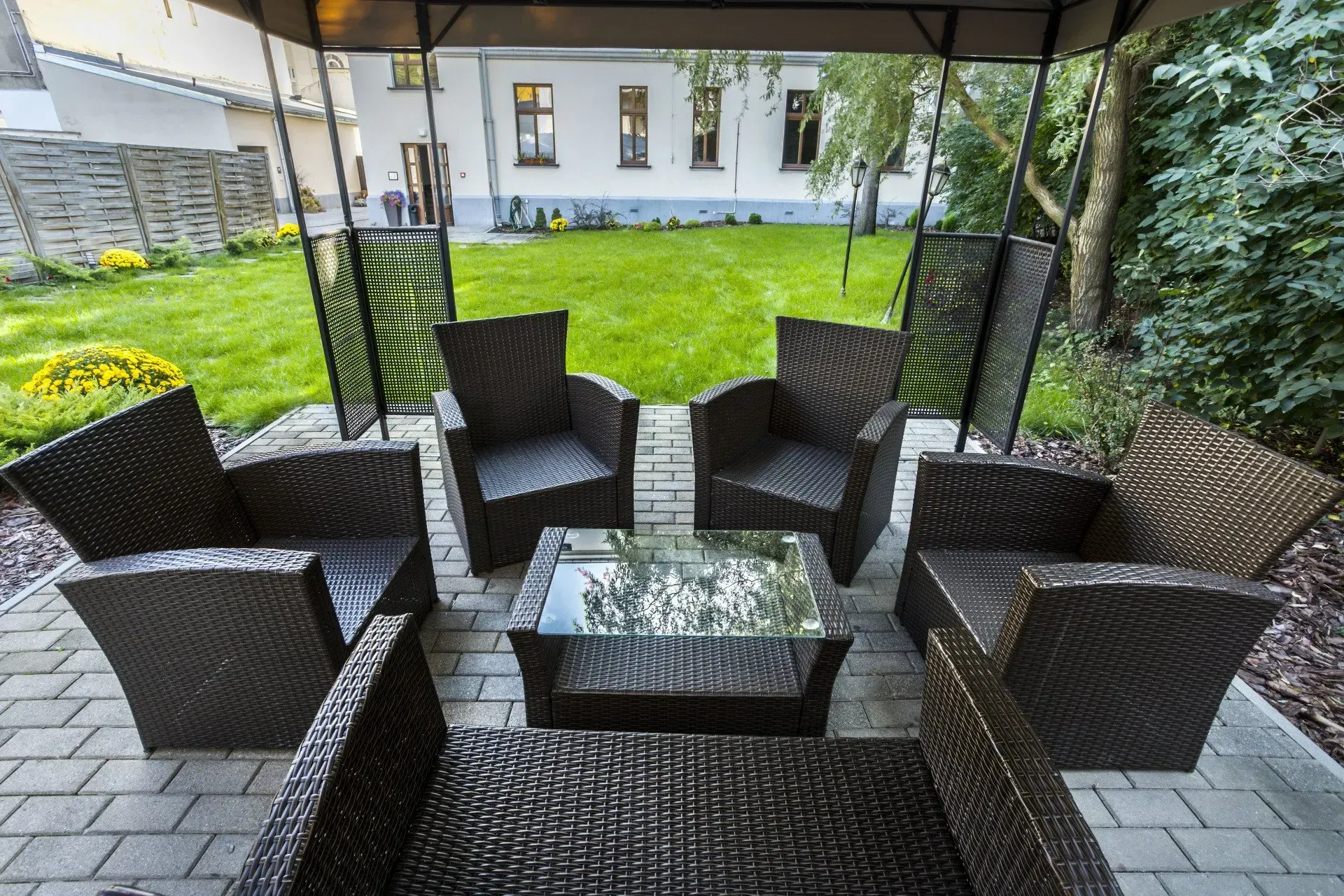 Outdoor patio seating area with wicker chairs and glass table under a gazebo on a paved terrace