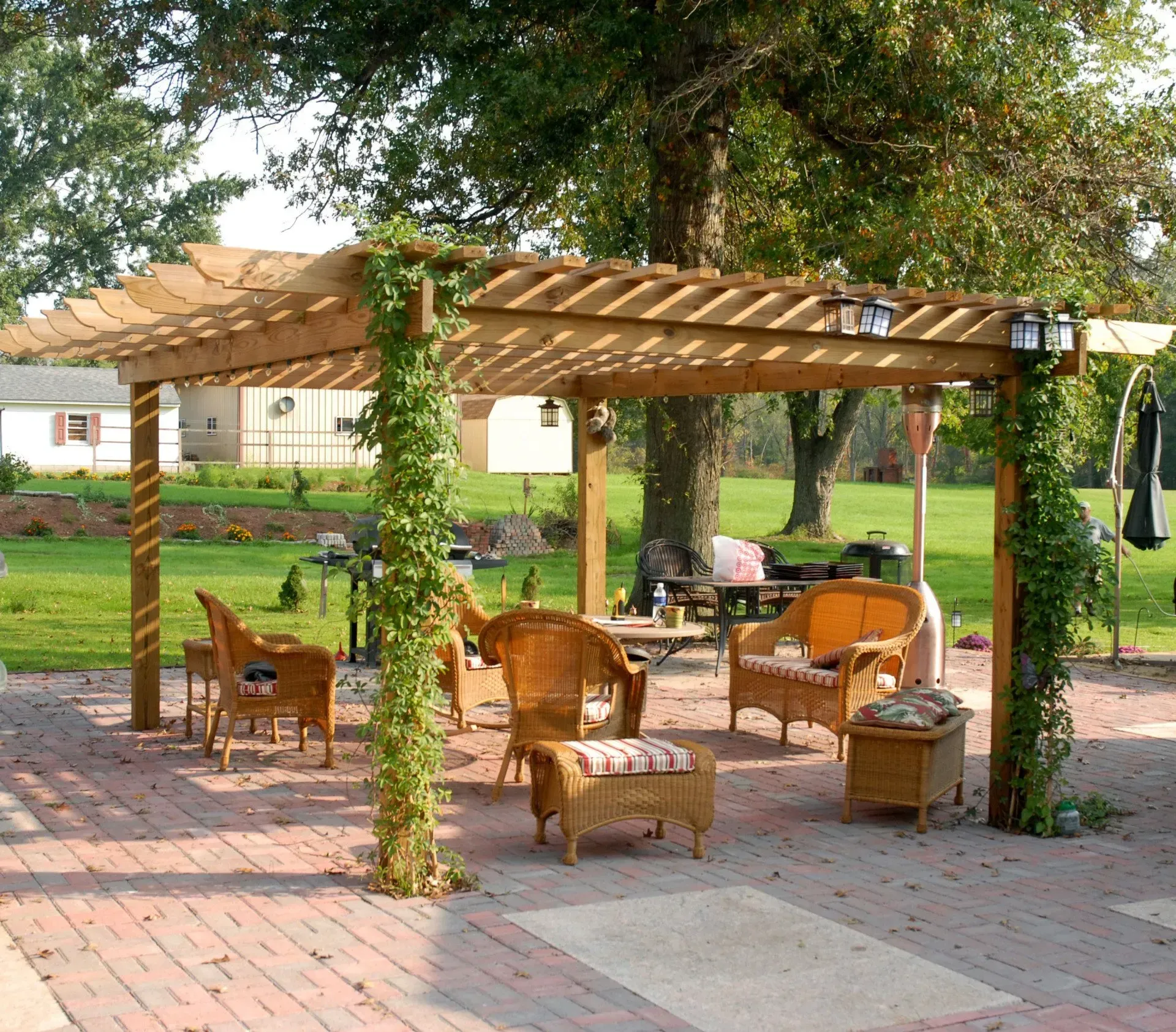Wooden pergola with outdoor seating on a brick patio in a park-like garden