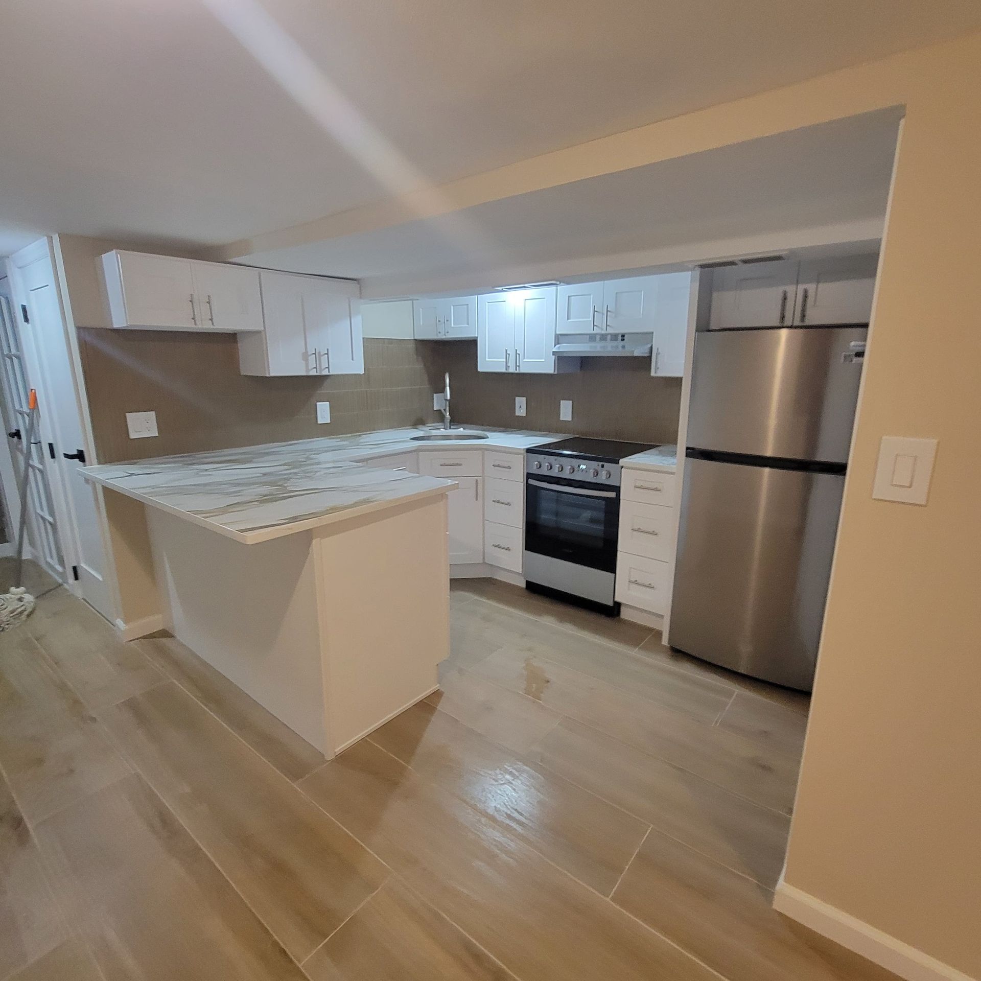 A newly renovated kitchen with white cabinets, stainless steel appliances, and light wood-look flooring.