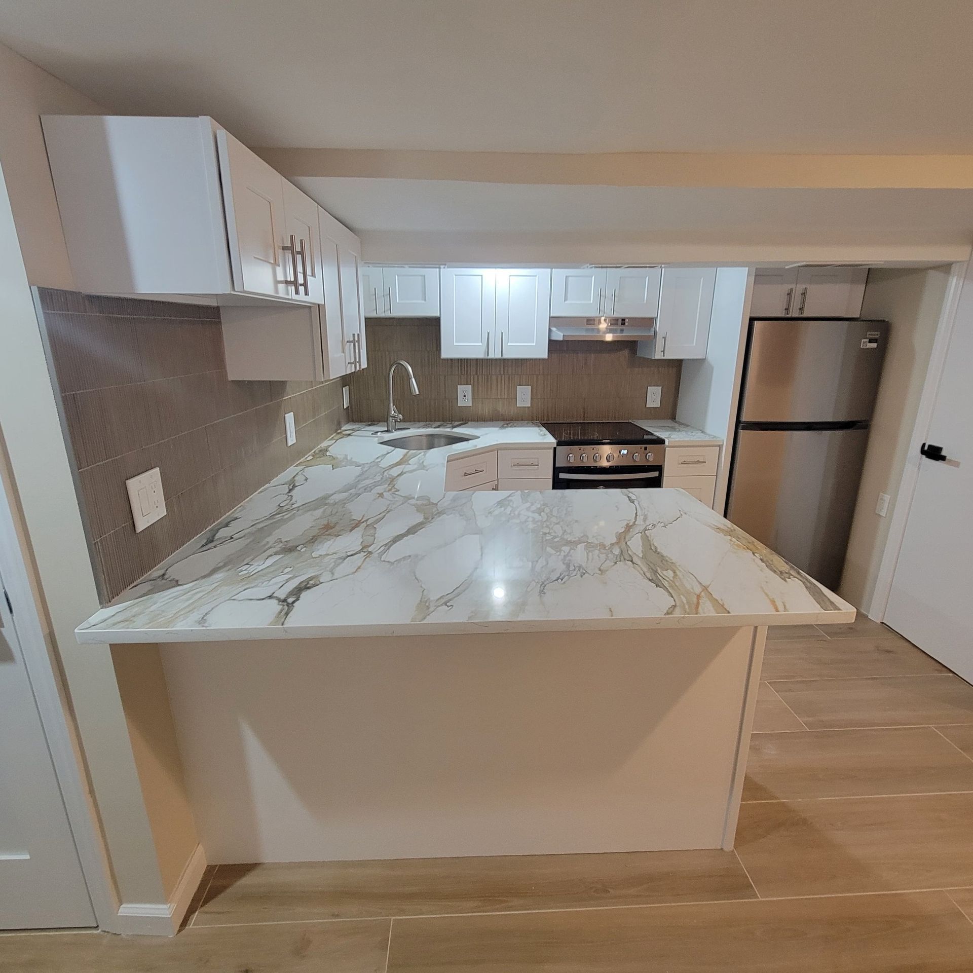 Modern kitchen with white cabinets, marble countertop island, stainless steel appliances.