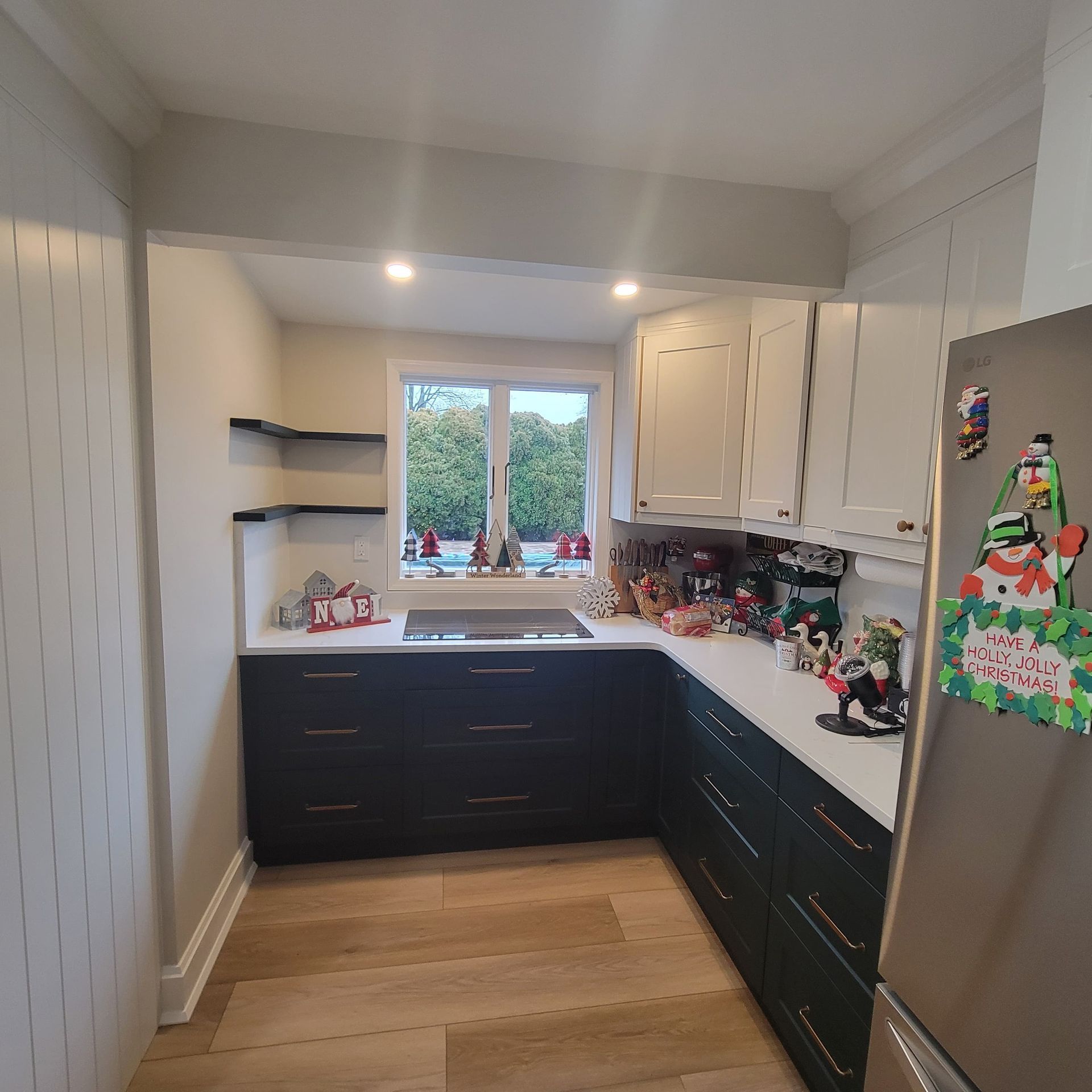 Kitchen with dark cabinets, white countertops, and white upper cabinets.  A window is centered.