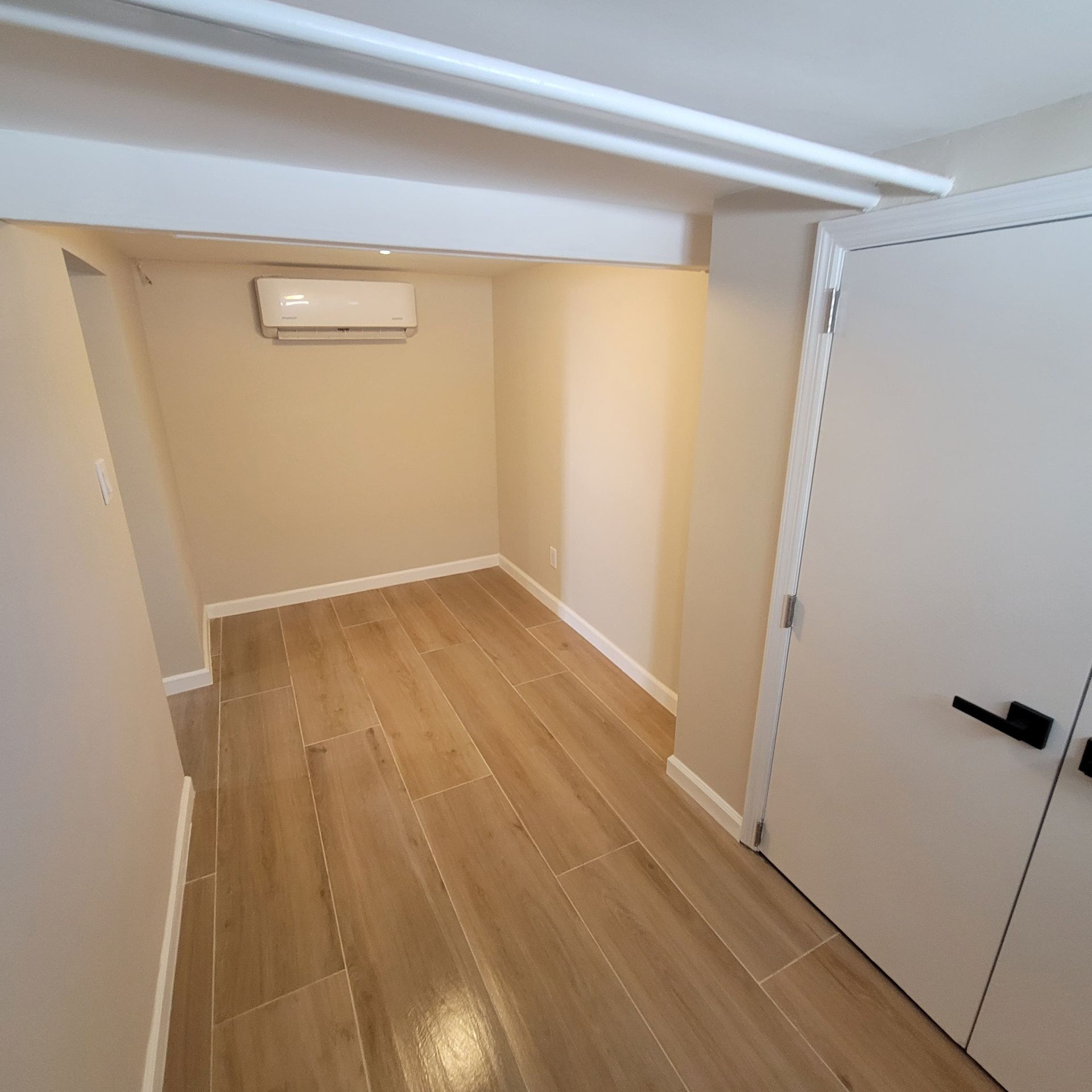 Empty room with wood-look tile floor, beige walls, white trim, and a closed door on the right.