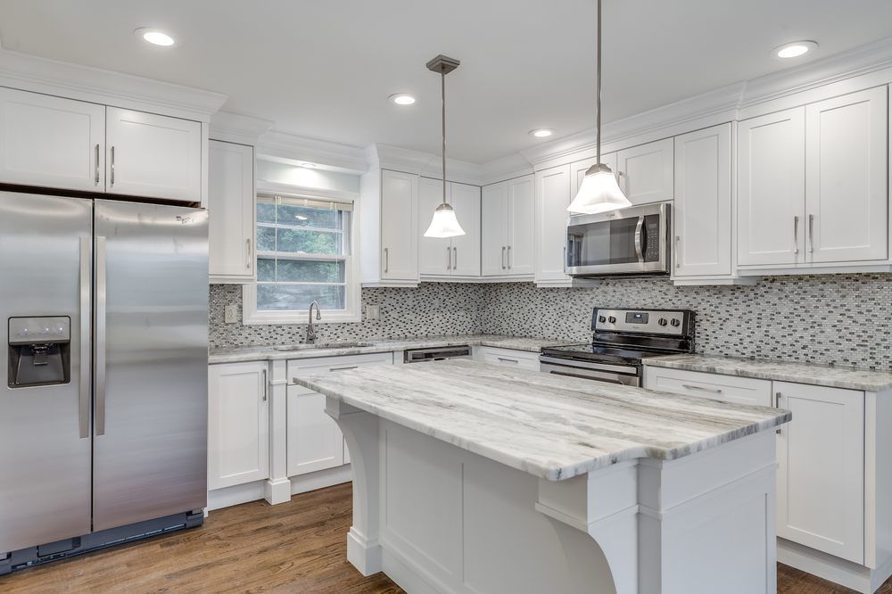 White kitchen with stainless steel appliances, marble countertops, and a mosaic tile backsplash.