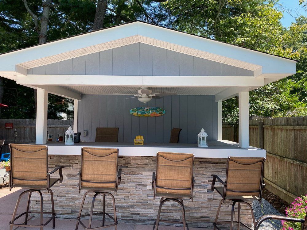 Outdoor bar with stone facade, light blue siding, and a white trim. Four bar stools face the bar.