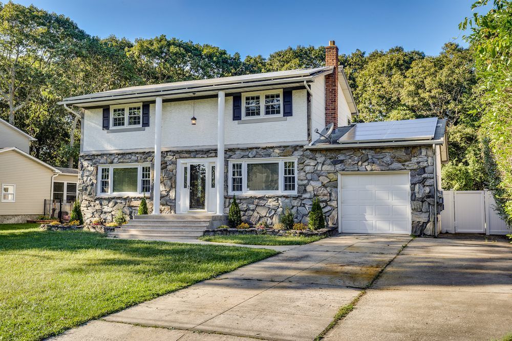 Two-story house with stone facade and attached garage. White siding, black shutters, green lawn, and a concrete driveway.