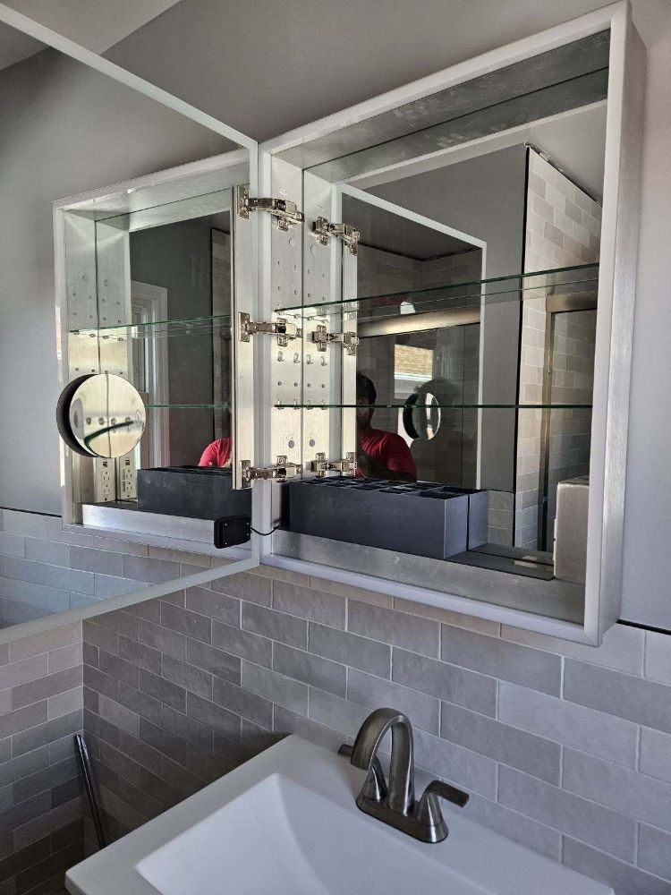 Double-door mirrored medicine cabinet in a bathroom, reflecting the sink, faucet, and tile backsplash.