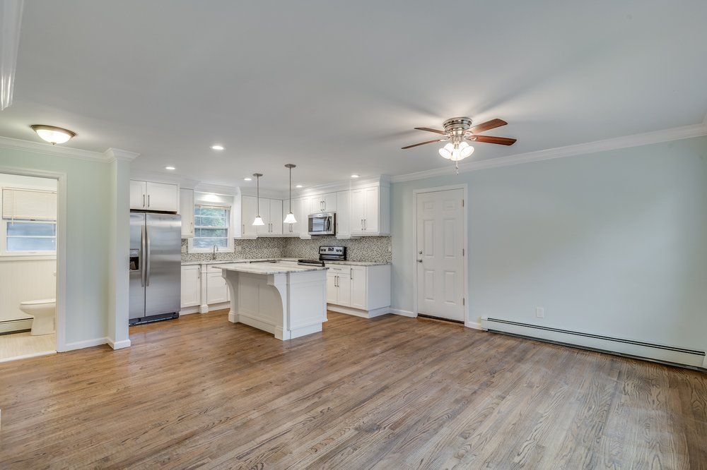 Open-concept kitchen and living area with hardwood floors and white cabinetry; the room has a light blue wall.