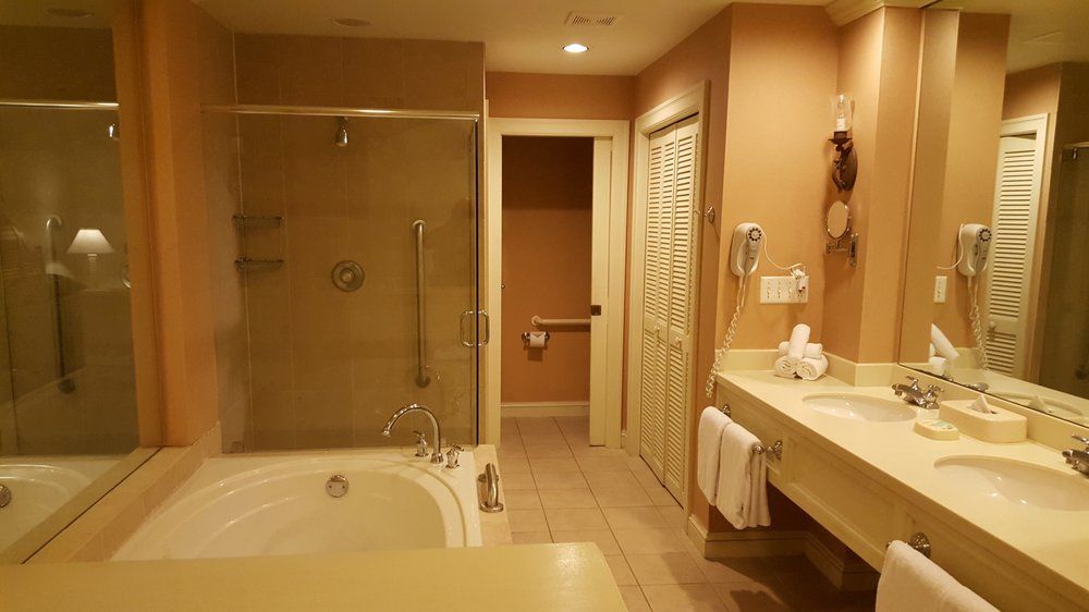 Spacious bathroom with a tub, shower, and double vanity. Light peach walls and cream-colored fixtures create a bright, warm atmosphere.