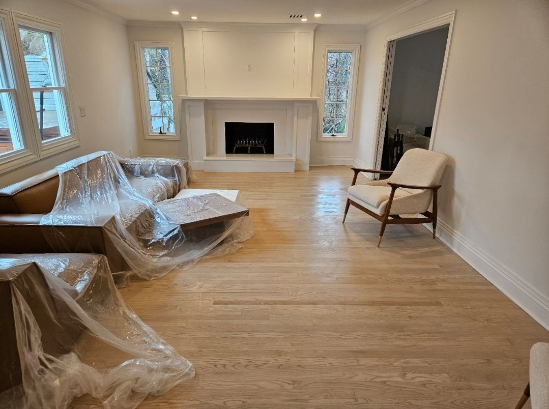 Living room with light wood floors, white walls, fireplace, and furniture covered in plastic.