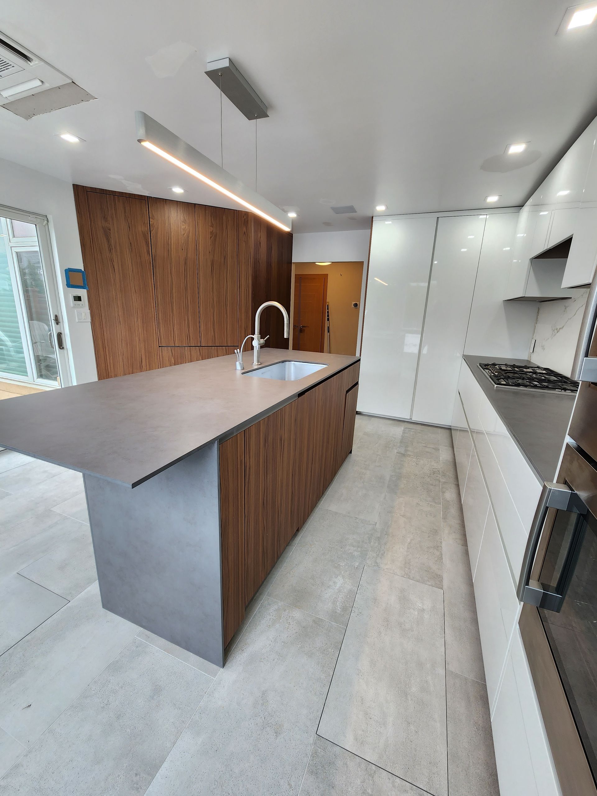Modern kitchen with a large island featuring a sink. Dark wood cabinets and a light countertop contrast with the light-colored floor and white cabinets.
