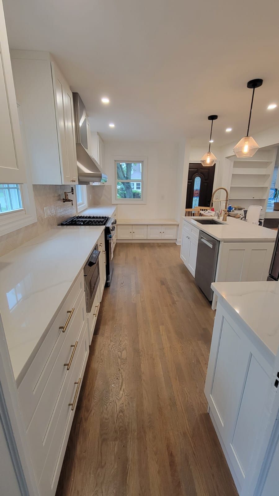 Bright kitchen with white cabinets, light countertops, and wooden floors. Island with sink, stainless steel appliances, and recessed lighting.