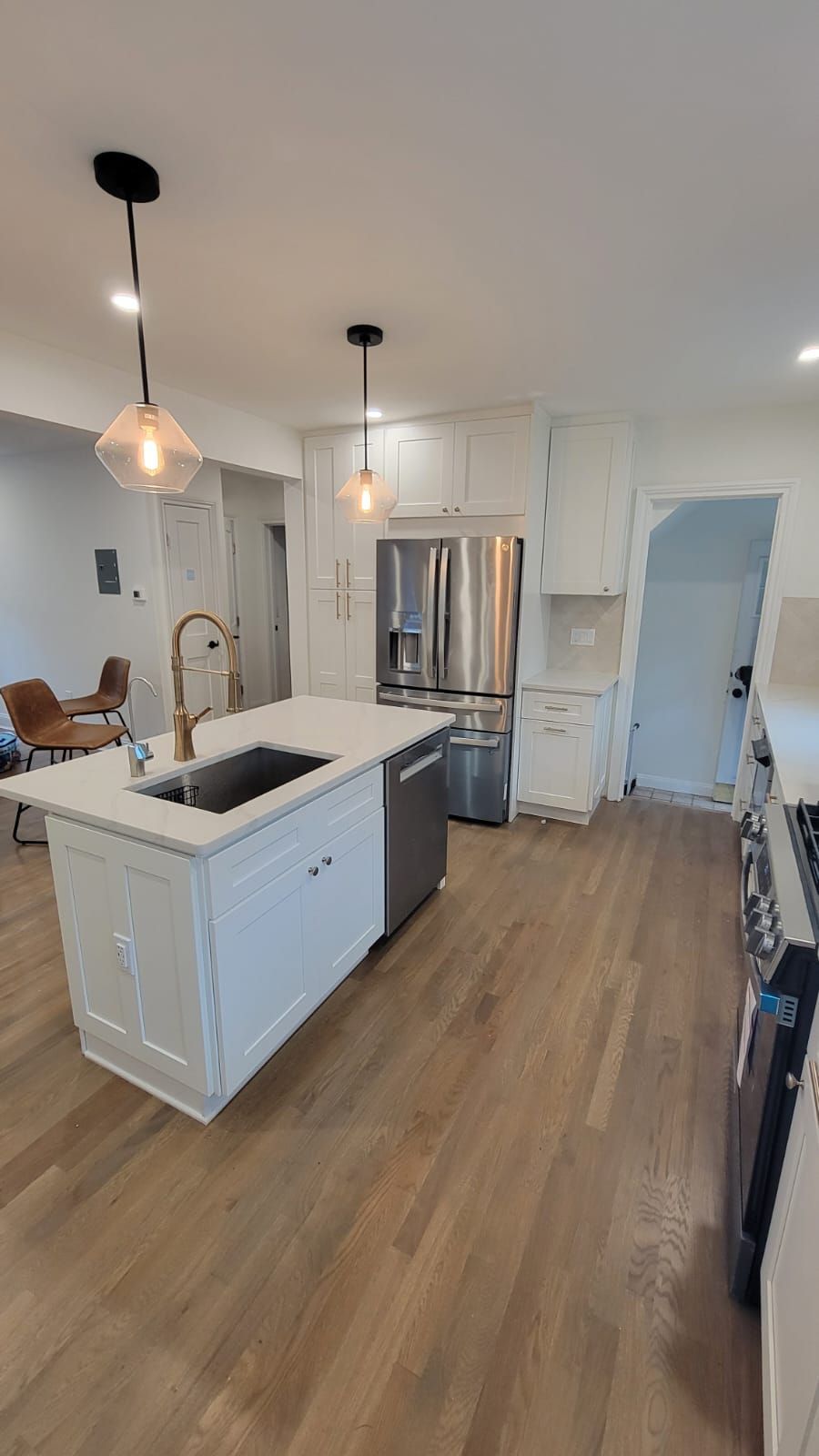 Modern kitchen with white cabinets, island with sink, stainless steel appliances, and hardwood floors.