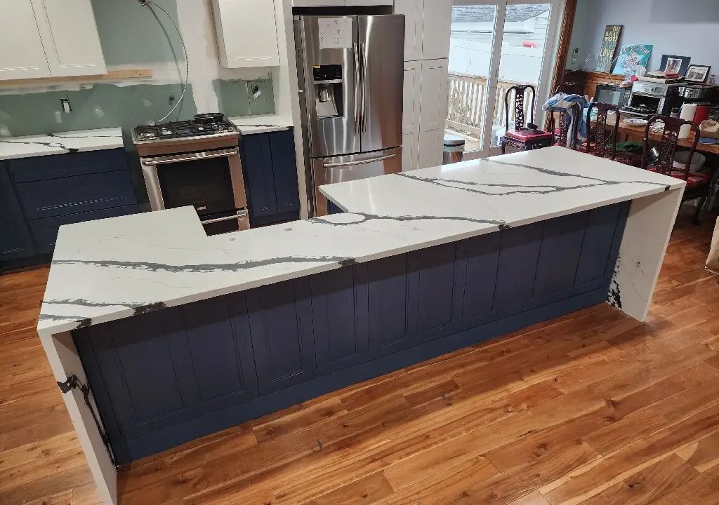 A kitchen under renovation features a navy blue island with white quartz countertops and veining, set against a wooden floor.
