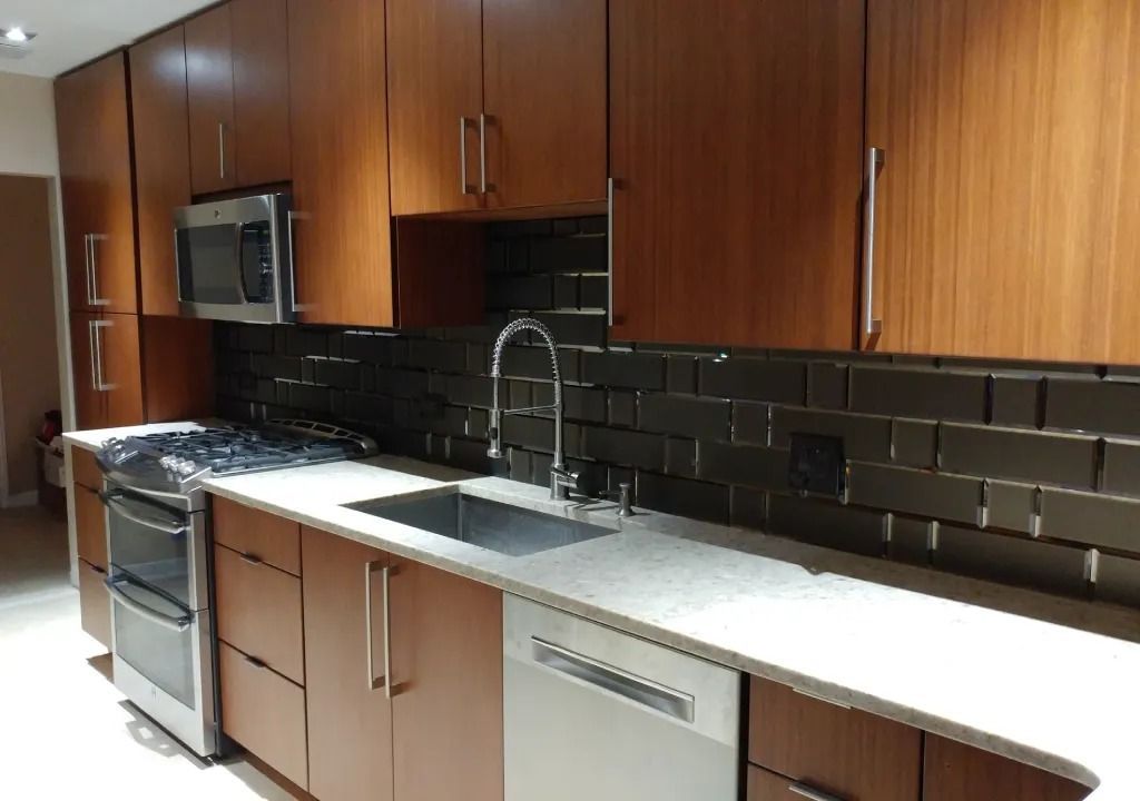 Modern kitchen with dark wood cabinets, stainless steel appliances, and a gray countertop with a dark backsplash.