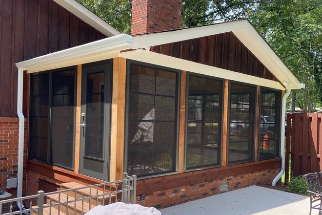 Screened porch attached to a brick house with a dark door, brown walls, and black screens.