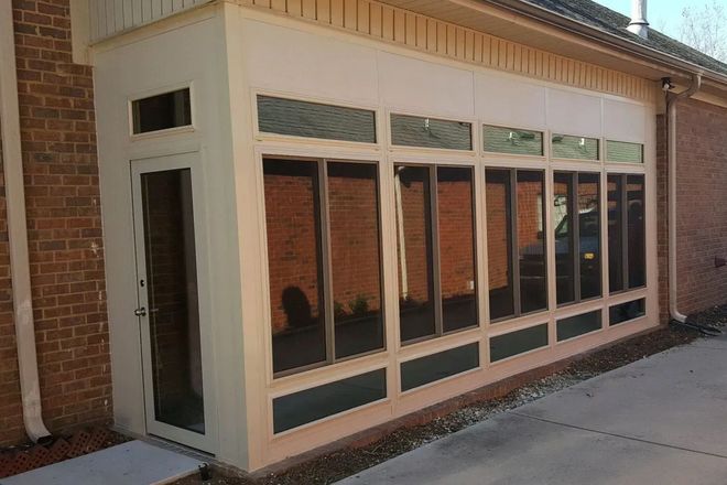 Sunroom with glass windows and door attached to a brick building.