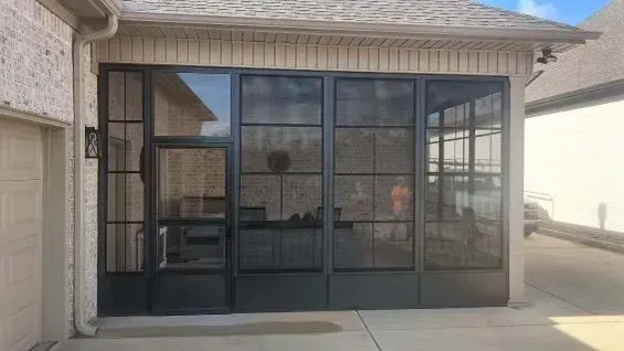 Screened-in porch with black metal frame, attached to house with a garage, concrete floor.
