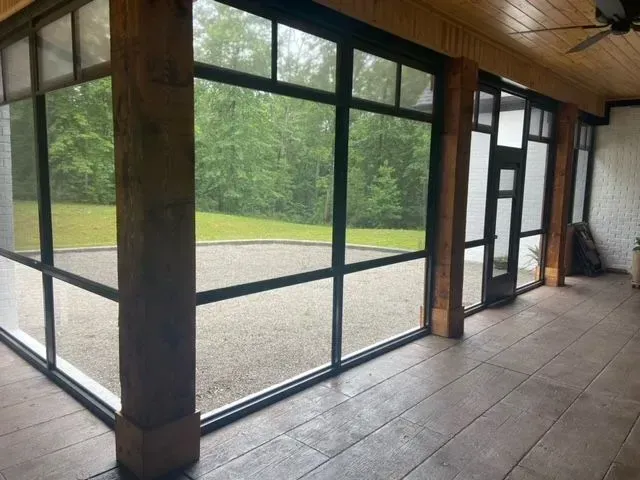Enclosed porch with large screened windows, wooden pillars, and view of green yard.