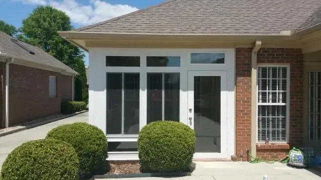 Exterior of a brick building with white framed windows and doors, green bushes in front.