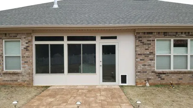 Back of a brick house with a sunroom addition, a pathway leads to the sunroom door.