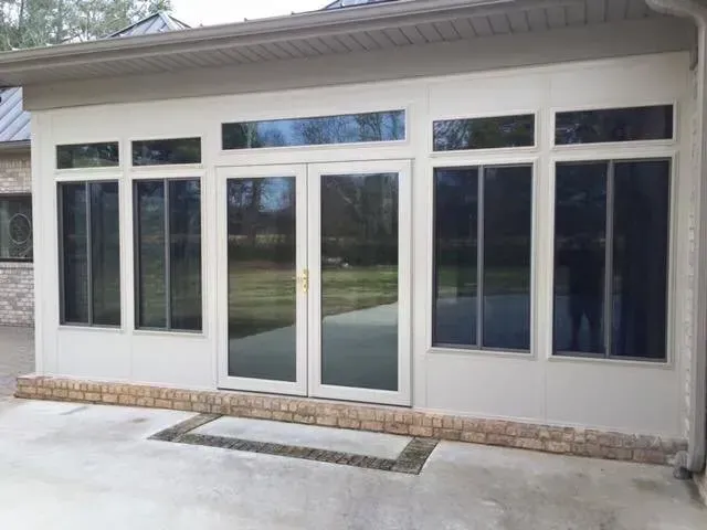 Sunroom with windows and glass doors, white exterior walls, and a brick base.