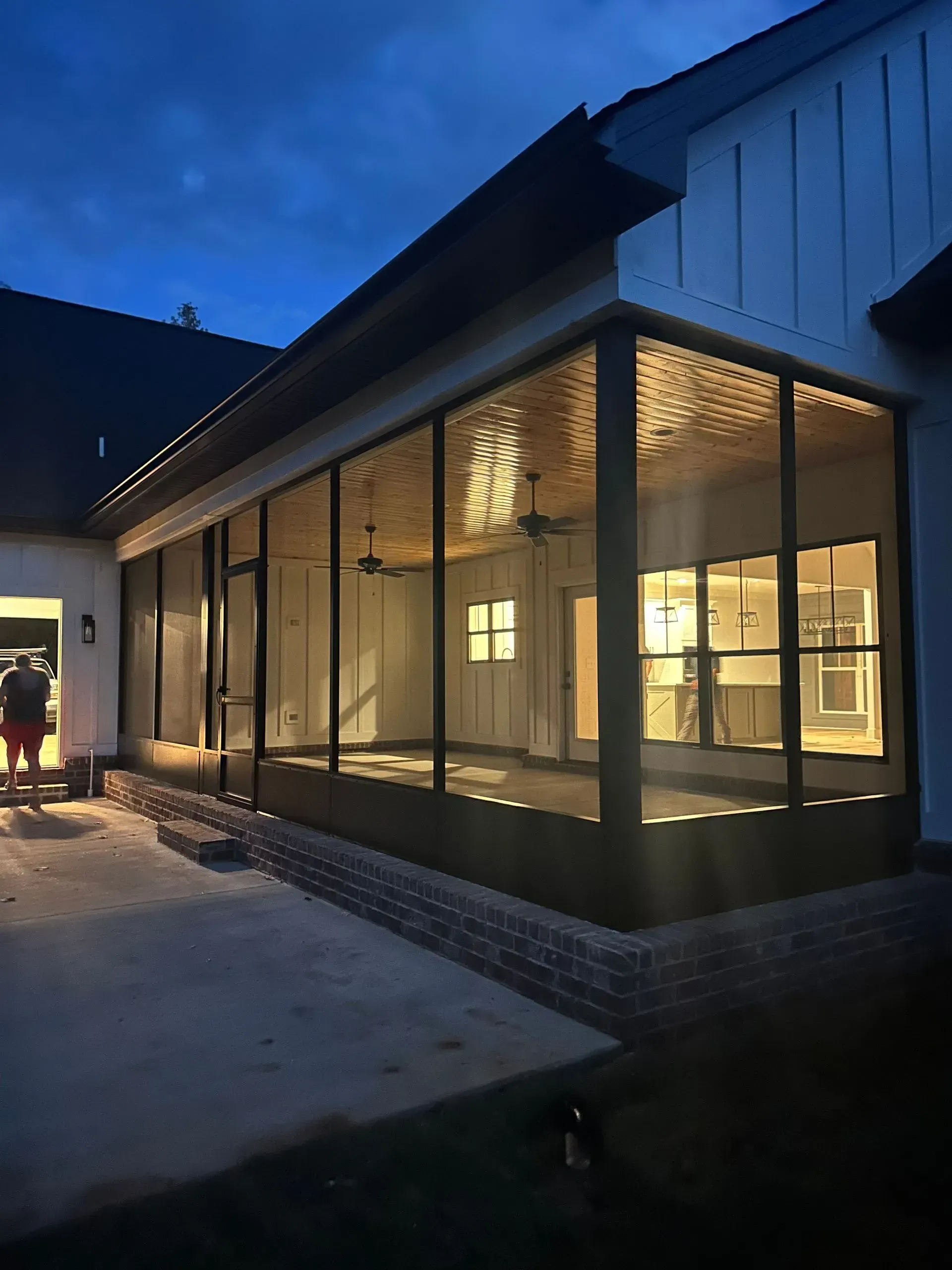 Screened-in porch at dusk, with interior lights on, brick base, and a dark roofline.