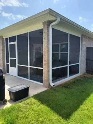 Screened-in porch with white frames, black screens, and a brick exterior.  It is on a concrete patio and has green grass.