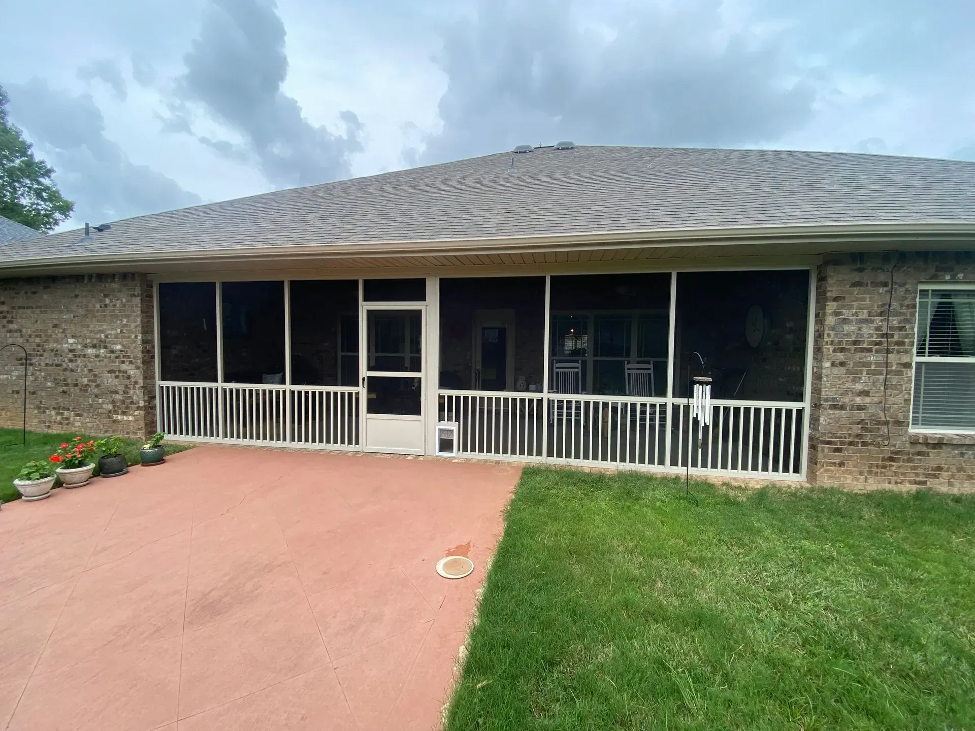 Screened-in porch with white railings, red patio, and brick exterior against a gray sky.