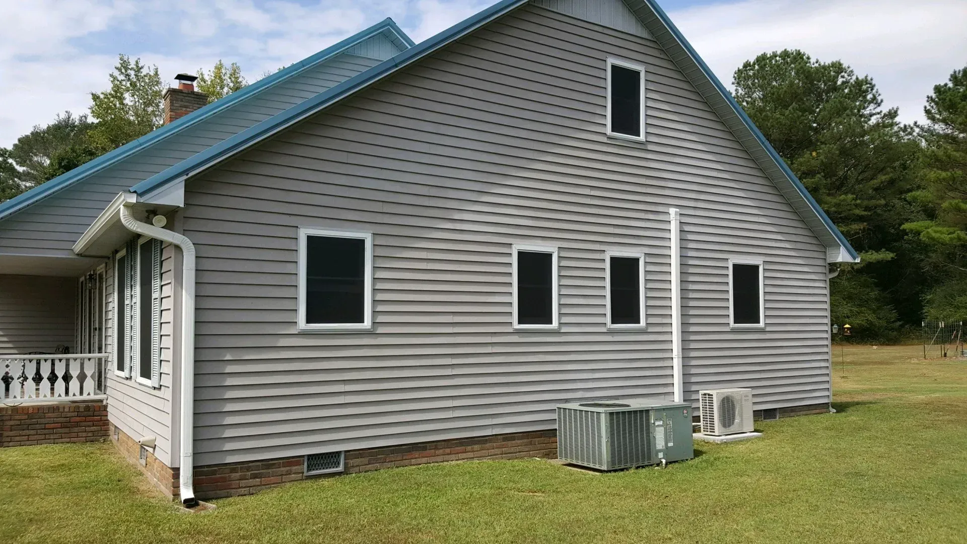 Side view of a gray house with white-framed windows, blue roof, and air conditioning unit.