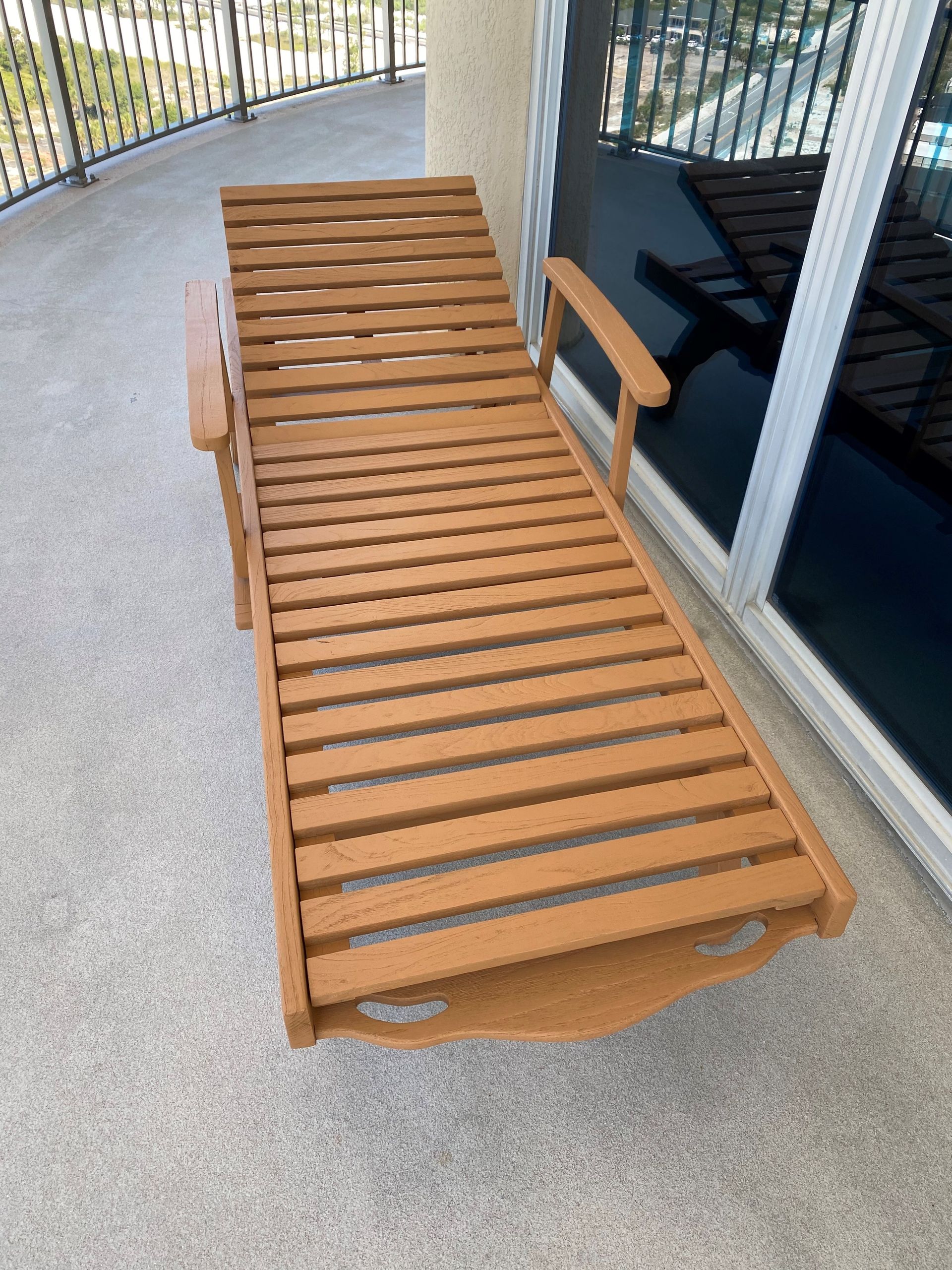 A wooden lounge chair is sitting on a balcony next to a sliding glass door.