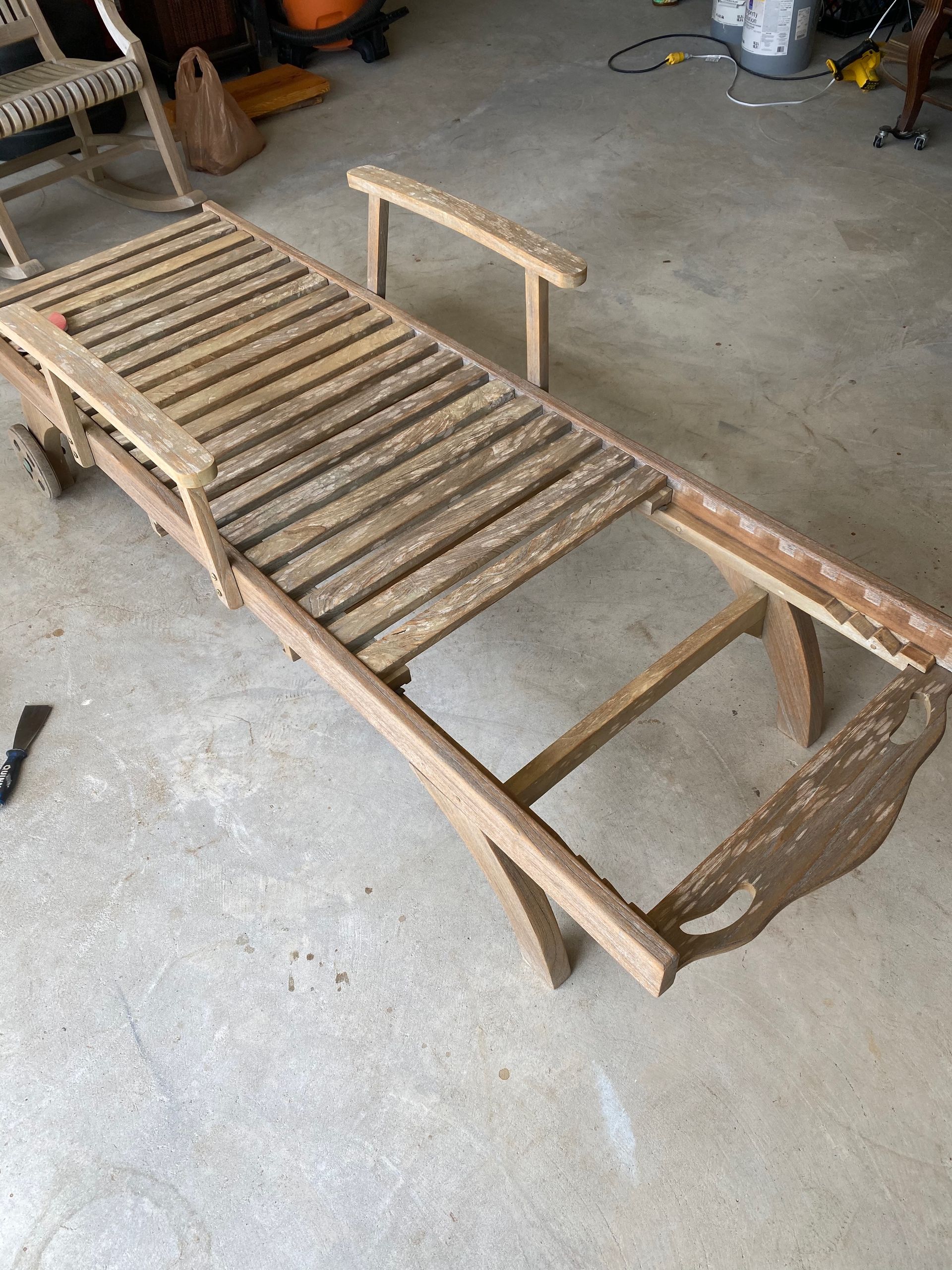 A wooden chaise lounge is sitting on the floor in a garage.