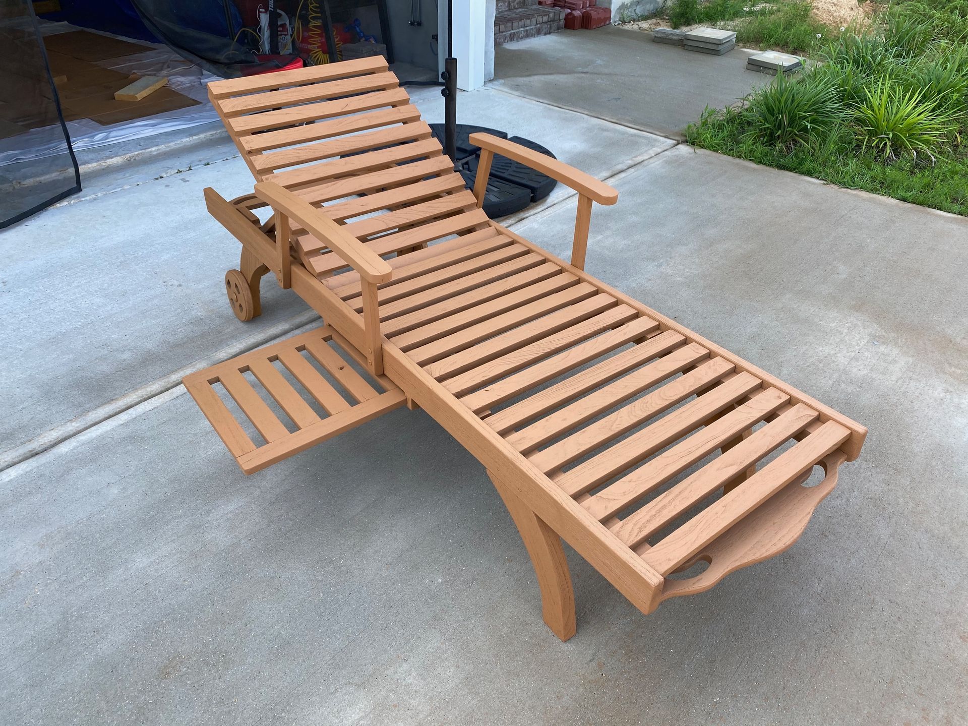 A wooden lounge chair is sitting on a concrete patio