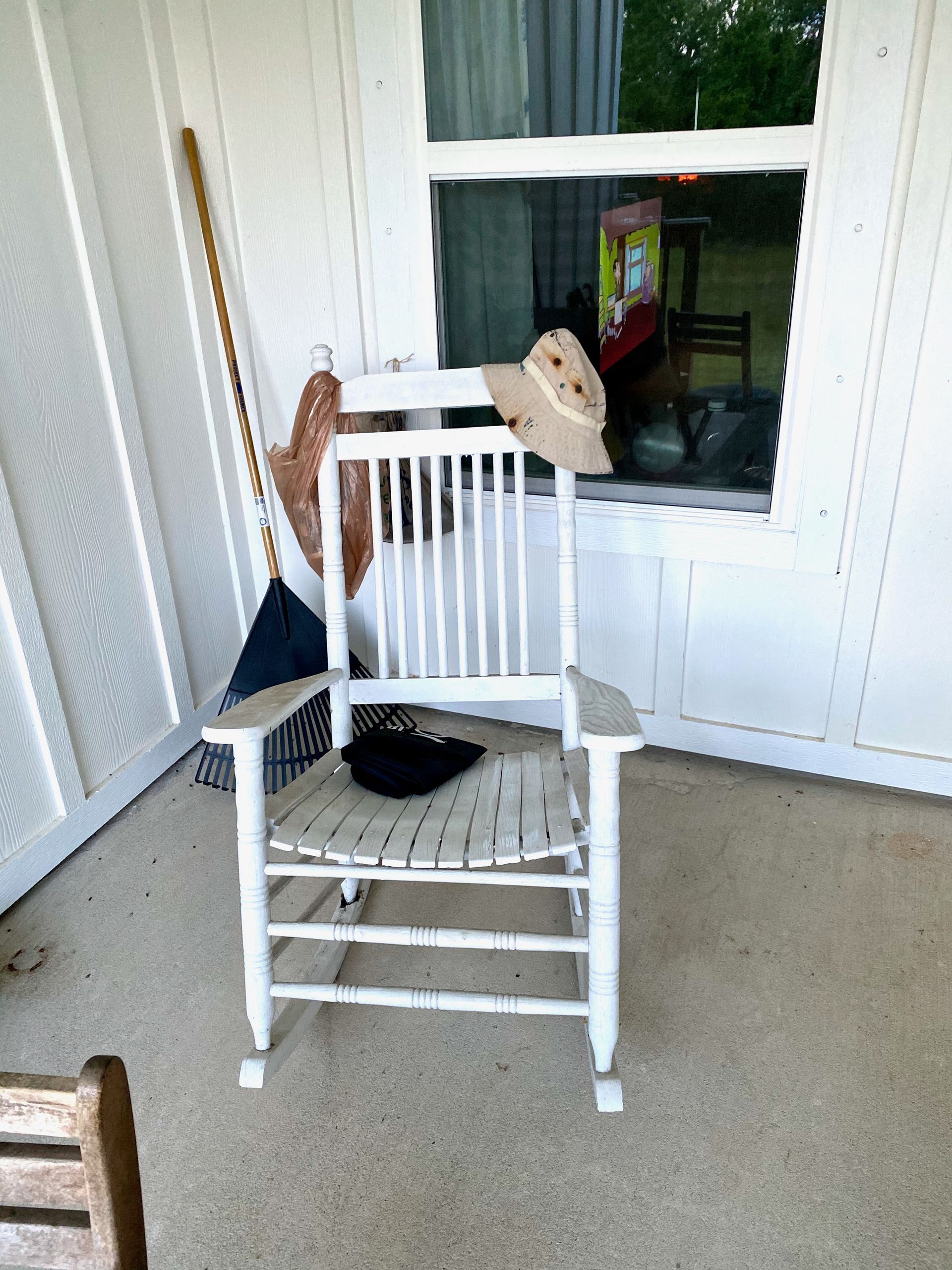 A white rocking chair on a porch with a hat on it