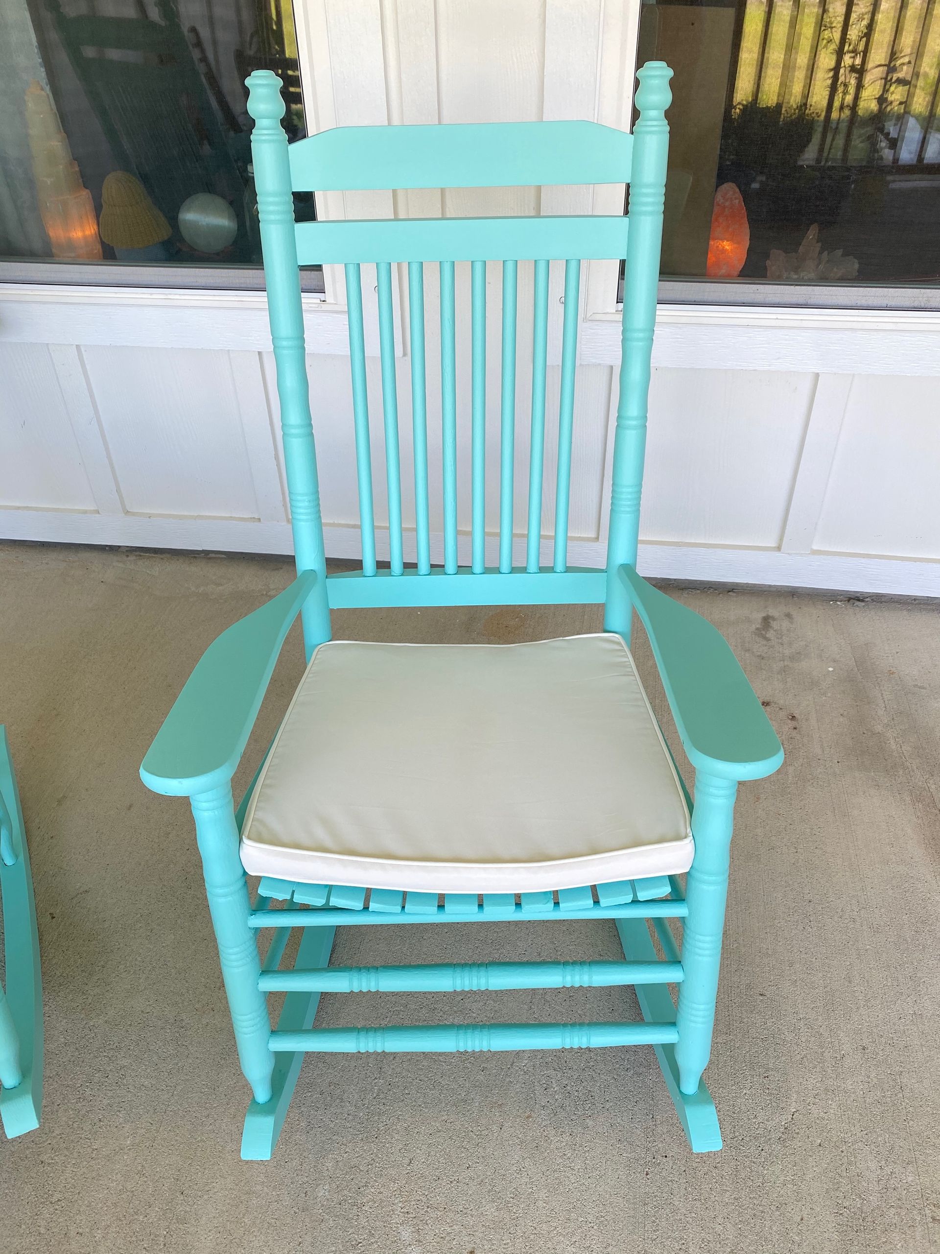 A blue rocking chair with a white cushion is sitting on a porch.
