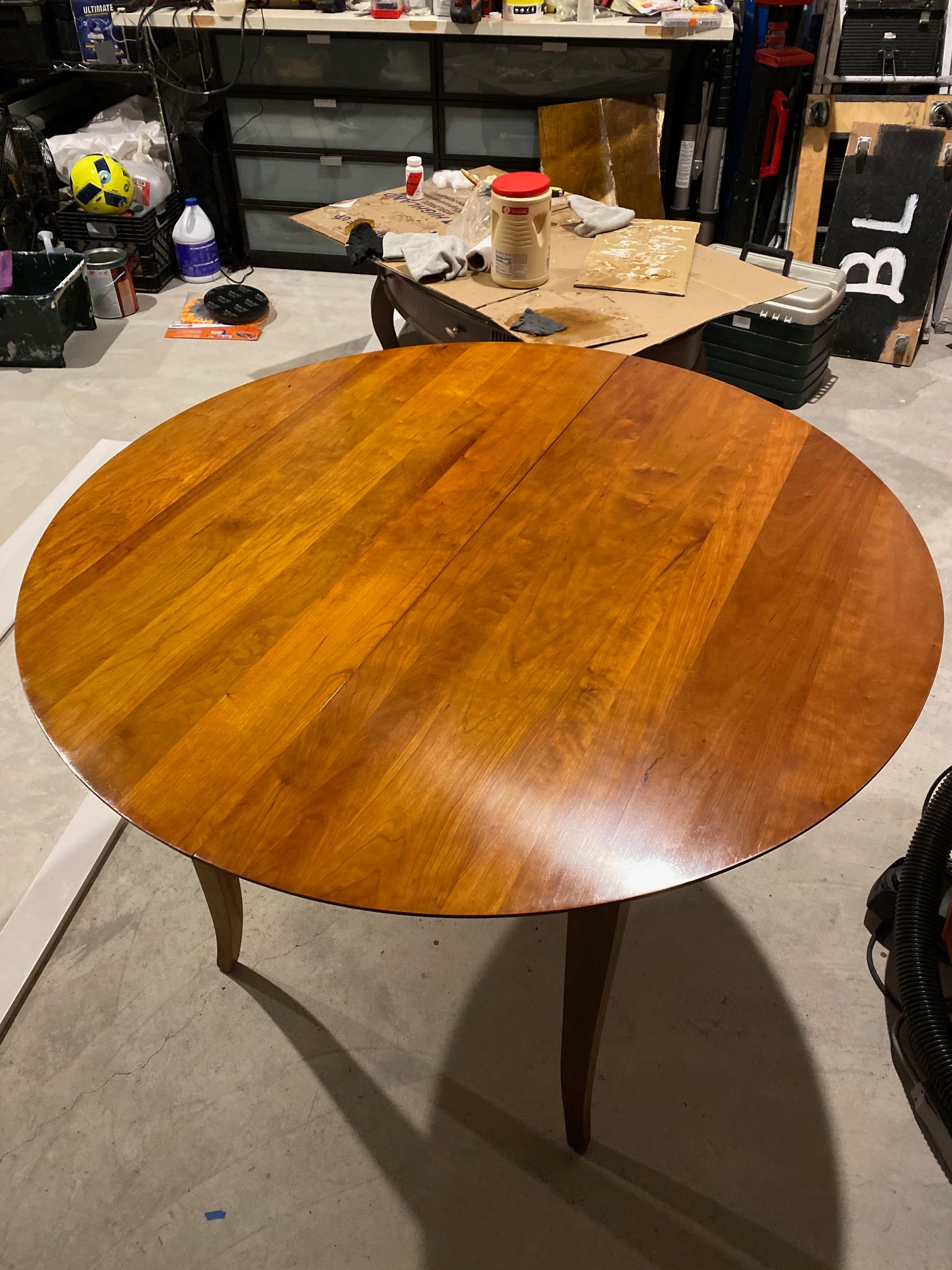 A round wooden table is sitting in a messy room.