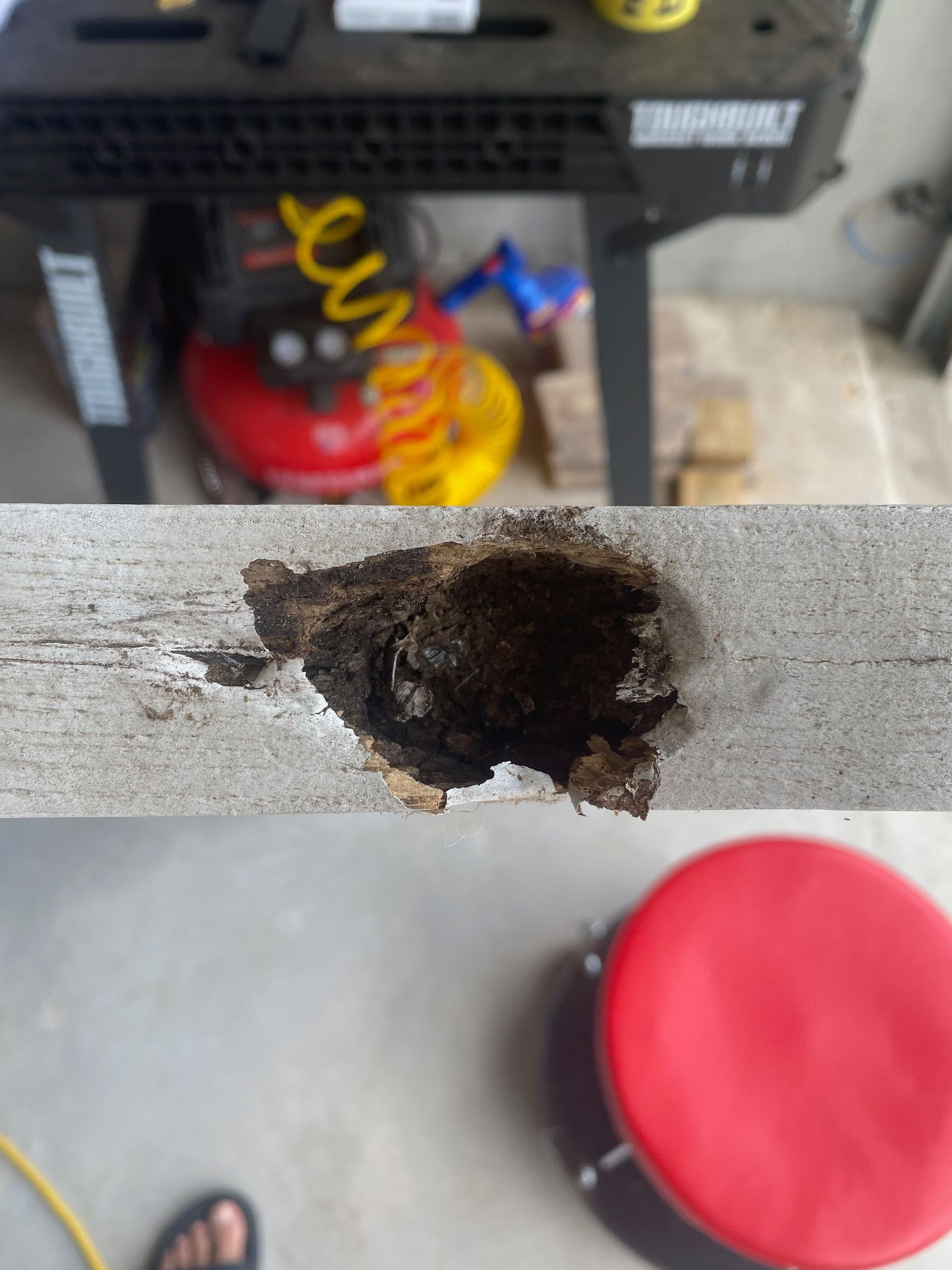 A hole in a piece of wood next to a red stool