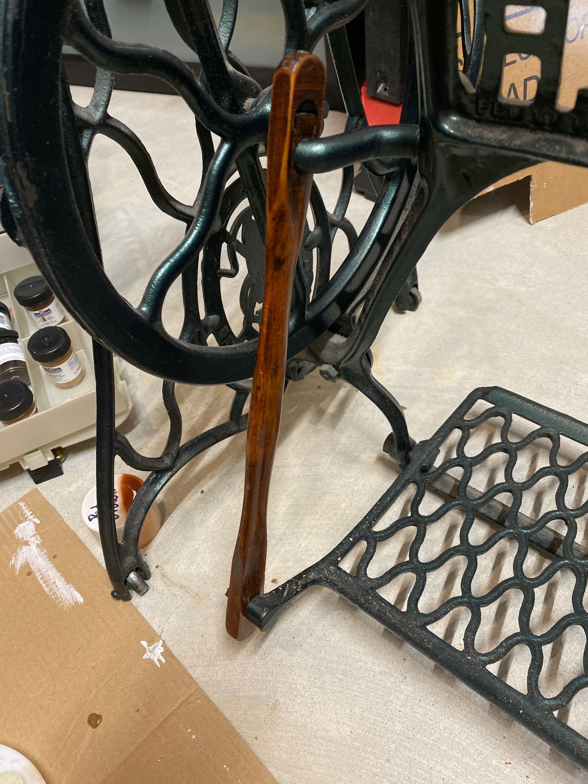 A sewing machine with a wooden leg is sitting on the floor.