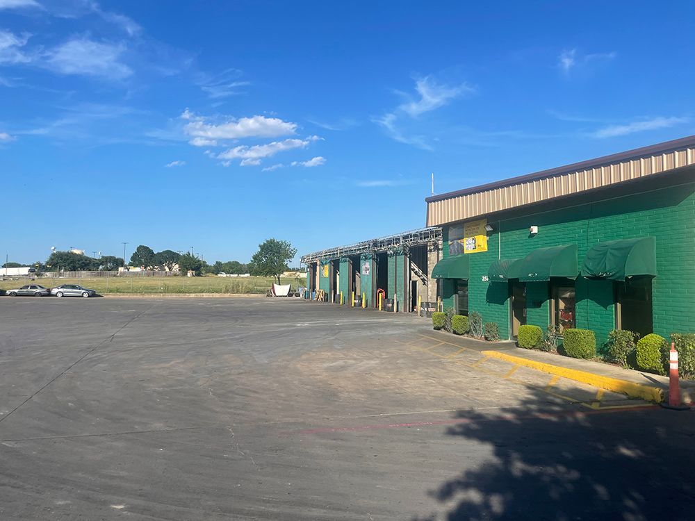 A green building with awnings on the windows is sitting in a parking lot.