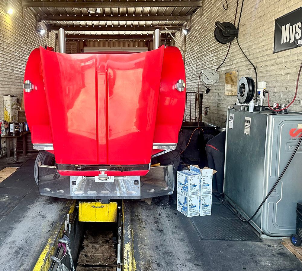 A red truck is parked in a garage next to a sign that says mustang